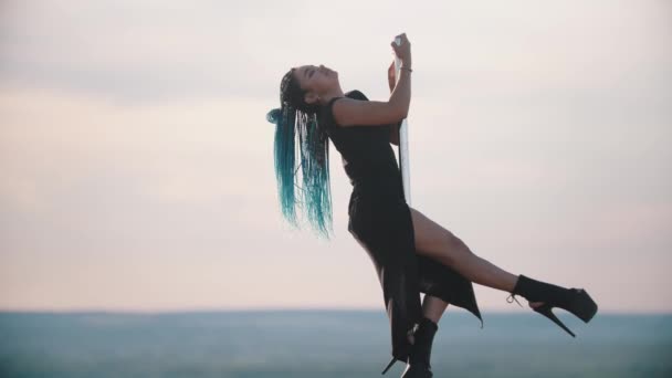 Жінка з блакитними косами на високих підборах танцює на верхній частині танцюючого полюса і спускається вниз — стокове відео