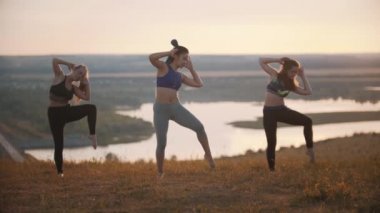 Dışarıda aerobik yapan üç genç kadın.