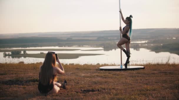 Femme prenant une photo d'une autre femme debout près du poteau de danse — Video