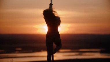 Açık spor elbiseli kadın gün batımında direğin yanında dans ediyor.