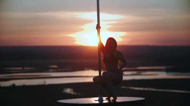 Egy nő nyitott sportruhában táncol a rúd mellett naplementekor. — Stock videók