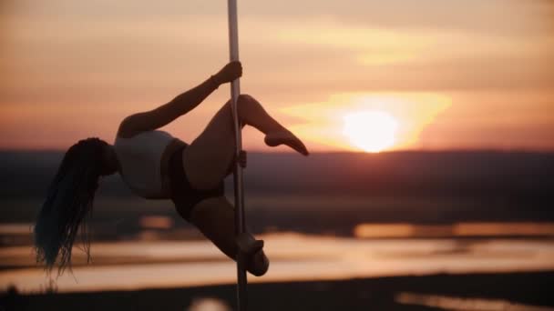 Ung kvinna med långa flätor dansar och snurrar på stolpen vid solnedgången — Stockvideo