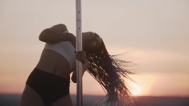 Jonge vrouw met lange vlechten dansen door de paal op zonsondergang avond — Stockvideo