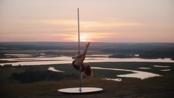 Jonge vrouw danser in sport kleding vasthouden door de paal met haar benen op zonsondergang — Stockvideo