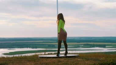 Doğada direk dansı. Neon yeşil mayolu seksi çekici kadın direğin yanında dans ediyor.