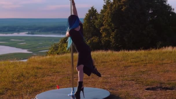 Pole dance na přírodě - sexy žena s dlouhými modrými copánky v černém oblečení spinning na tyči na sobě vysoké podpatky — Stock video