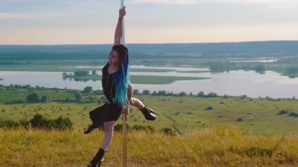 Танець полюса на природі сексуальна жінка з блакитними косами в чорному одязі, що крутиться на полюсі в високих підборах — стокове відео