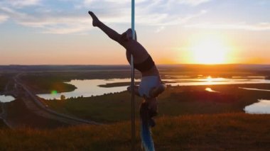 Doğada direk dansı. Gün batımında bacaklarıyla dans direğini tutan genç bir kadın.