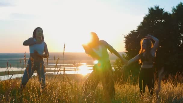Аэробика на природе - три девушки занимаются аэробикой и медленными движениями руками на закате — стоковое видео
