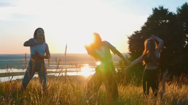 Aeróbicos en la naturaleza: tres jóvenes haciendo danza aeróbica y movimientos lentos con las manos al atardecer — Vídeo de stock