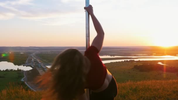 Taniec na rurze na zachodzie słońca - młoda kobieta w sportowej odzieży wirująca nad biegunem z rozłożonymi nogami — Wideo stockowe