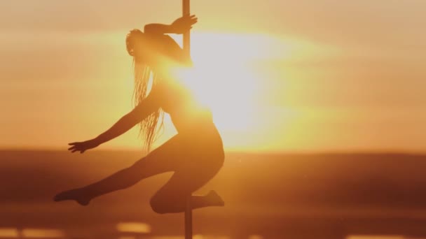 Танець полюса на яскравому заході сонця акробатична жінка крутиться на танцювальному полюсі — стокове відео