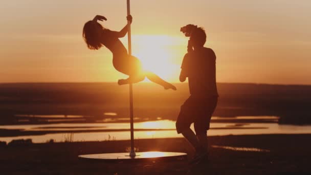 Pool dans op zonsondergang - jonge vrouw dansen op paal en operator filmen haar — Stockvideo