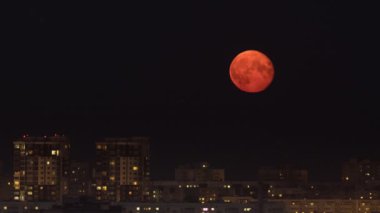 Parlak turuncu ay ve karanlık gece gökyüzü şehrin üzerinde.