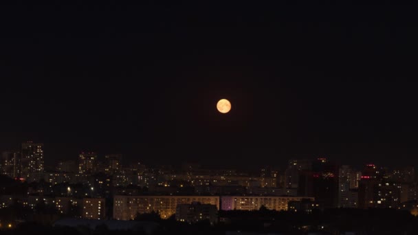 Jasně žlutý měsíc vychází na tmavé noční obloze nad městem — Stock video