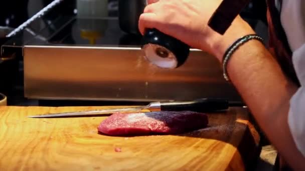 Cozinha restaurante - chef salgando o pedaço de carne na mesa — Vídeo de Stock