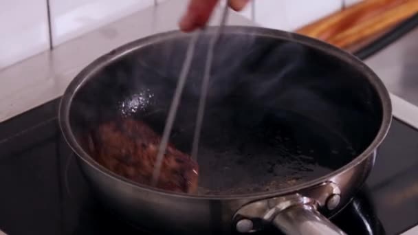 Dapur restoran koki sedang menggoreng steak dalam panci yang dalam dan memutarnya dengan tongkat — Stok Video