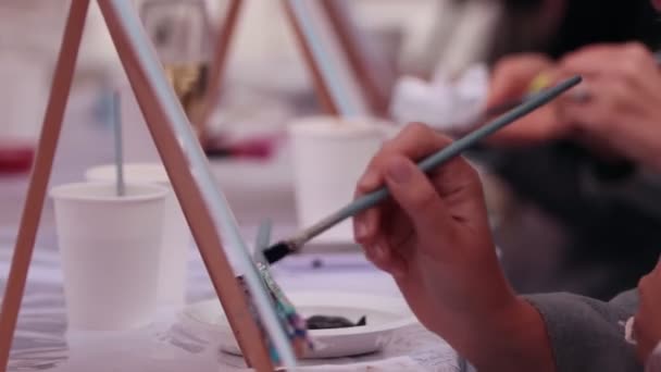 Несколько человек сидят в студии и рисуют на холстах кисточками — стоковое видео