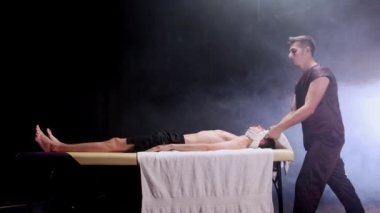 Karanlık stüdyoda masaj seansı. Masajcı müşterilerini havlularla boğuyor.