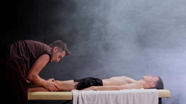 Massage session in dark studio - massagist massaging the mans knees — Stock Video