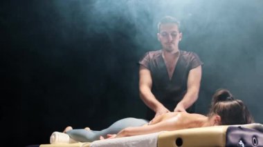 Koyu dumanlı stüdyoda masaj seansı. Erkek terapist kadınlara yağ ile masaj yapıyor.