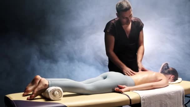 Sesión de masaje en estudio oscuro con iluminación brillante - terapeuta masajeando a las mujeres con aceite — Vídeo de stock