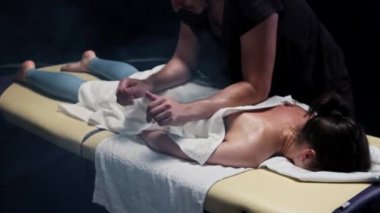 Dumanlı stüdyoda masaj seansı. Terapist, kadınlara havluyla masaj yapıyor.