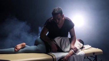 Dumanlı stüdyoda masaj seansı. Kadın vücuduna baskı yapan terapist.