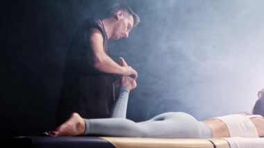 Dumanlı stüdyoda masaj seansı. Erkek terapist, genç kadınlara ayak masajı yapıyor.