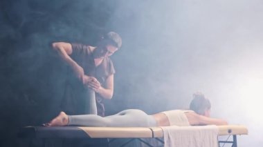 Siyah dumanlı stüdyoda masaj seansı. Genç kadınlara masaj yapan erkek terapist.