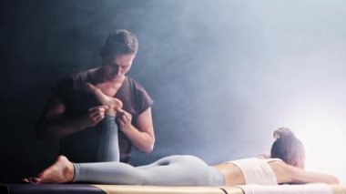 Siyah dumanlı stüdyoda masaj seansı. Genç kadınların ayak ve ayak bileklerine masaj yapan erkek terapist.