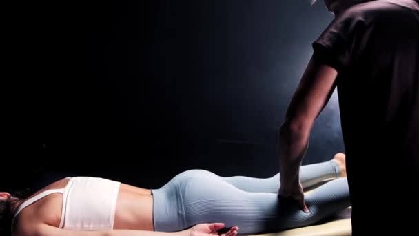 Séance de massage dans le studio sombre - massagiste déplaçant la jambe des femmes dans le genou — Video