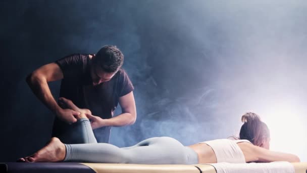 Massage sessie in de rokerige studio - lachende man therapeut masseren jonge vrouwen voet — Stockvideo