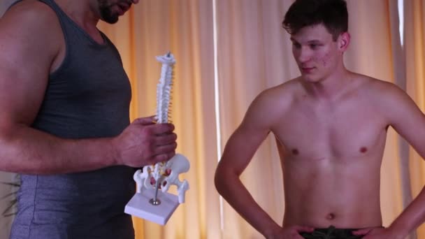 Sesja kręgarska w studio - lekarz trzymający plastikową próbkę ludzkiego kręgosłupa i rozmawiający ze swoim klientem — Wideo stockowe