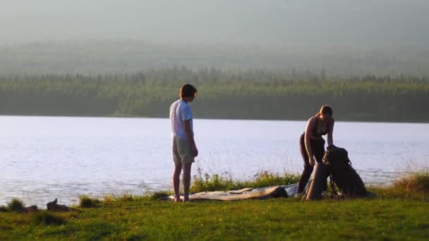 Unga par sätter upp ett tält nära floden — Stockvideo