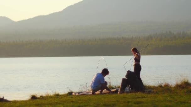 Молодая пара мужчин и женщин устанавливают палатку у реки — стоковое видео
