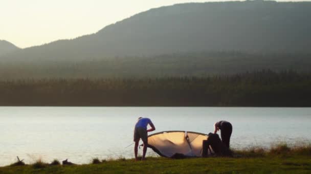 Jong stel zet een tent op bij de rivier bij zonsondergang — Stockvideo