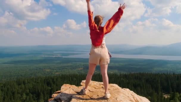 Fiatal nő áll a hegy szélén, és felemeli a kezét. — Stock videók