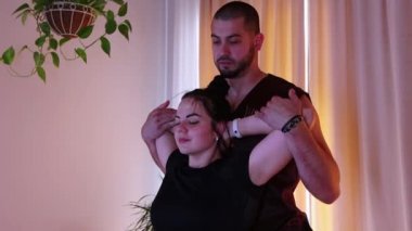 Stüdyoda kayropraktik seansı. Kanepede oturan kadın ve doktor dirseklerini tutup kendine doğru itiyor.