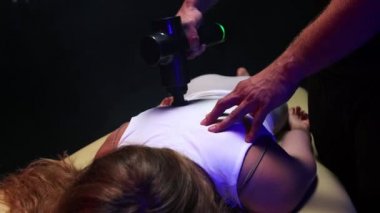 Kayropraktik terapi. Genç bir kadının sırtına bir aletle masaj yapan bir erkek terapist.