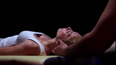 Karanlık stüdyoda kayropraktik terapi. Genç bir kadının boynunu rahatlatan bir erkek terapist.