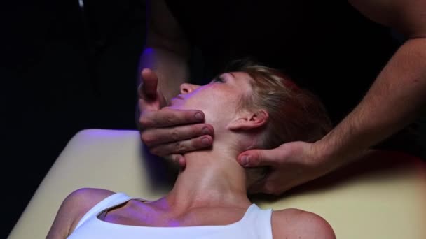 Kiropraktisk terapi i den mörka studion - en manlig terapeut som slappnar av i nacken på den unga kvinnan och får henne att vända sig åt sidan — Stockvideo