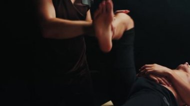 Karanlık stüdyoda kiropraktik terapi. Müvekkilinin ayak eklemlerini ısıtan bir terapist.