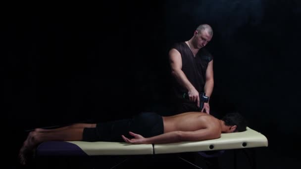 Thérapie chiropratique dans le studio sombre - un thérapeute masculin massant le dos de son client à l'aide d'un appareil — Video