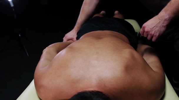 Terapia quiroprática no estúdio escuro - um terapeuta colocando uma mão de seu cliente atrás de suas costas e massageando sua lâmina — Vídeo de Stock