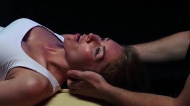 Karanlık stüdyoda kayropraktik terapi. Bir adam kadının omurgasını yerleştiriyor ve kadın gülümsüyor.