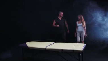 Karanlık stüdyoda kiropraktik terapi. Terapist ve kadın müşterisi kanepede yürüyorlar ve birbirleriyle konuşuyorlar.