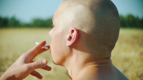 En skallig man sitter på planen och röker en cigarett — Stockvideo