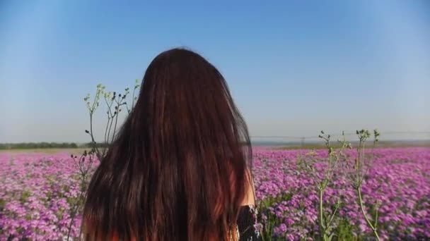 Ung kvinna i klänning går på blomman fältet och vänder tillbaka tittar in i kameran — Stockvideo