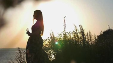 Günbatımında doğada duran, bol elbiseli romantik bir kadın.